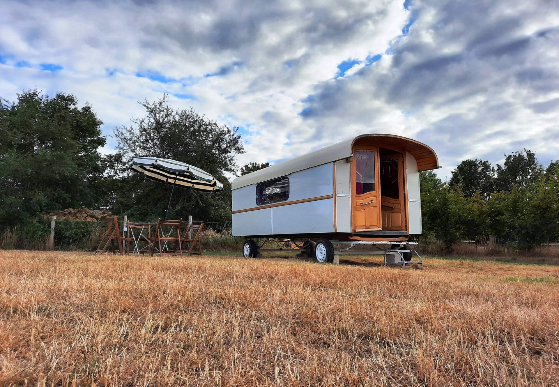 Roulotte Gitane 2 Caravane vintage dans un champ, avec une table et un parasol pour se détendre.