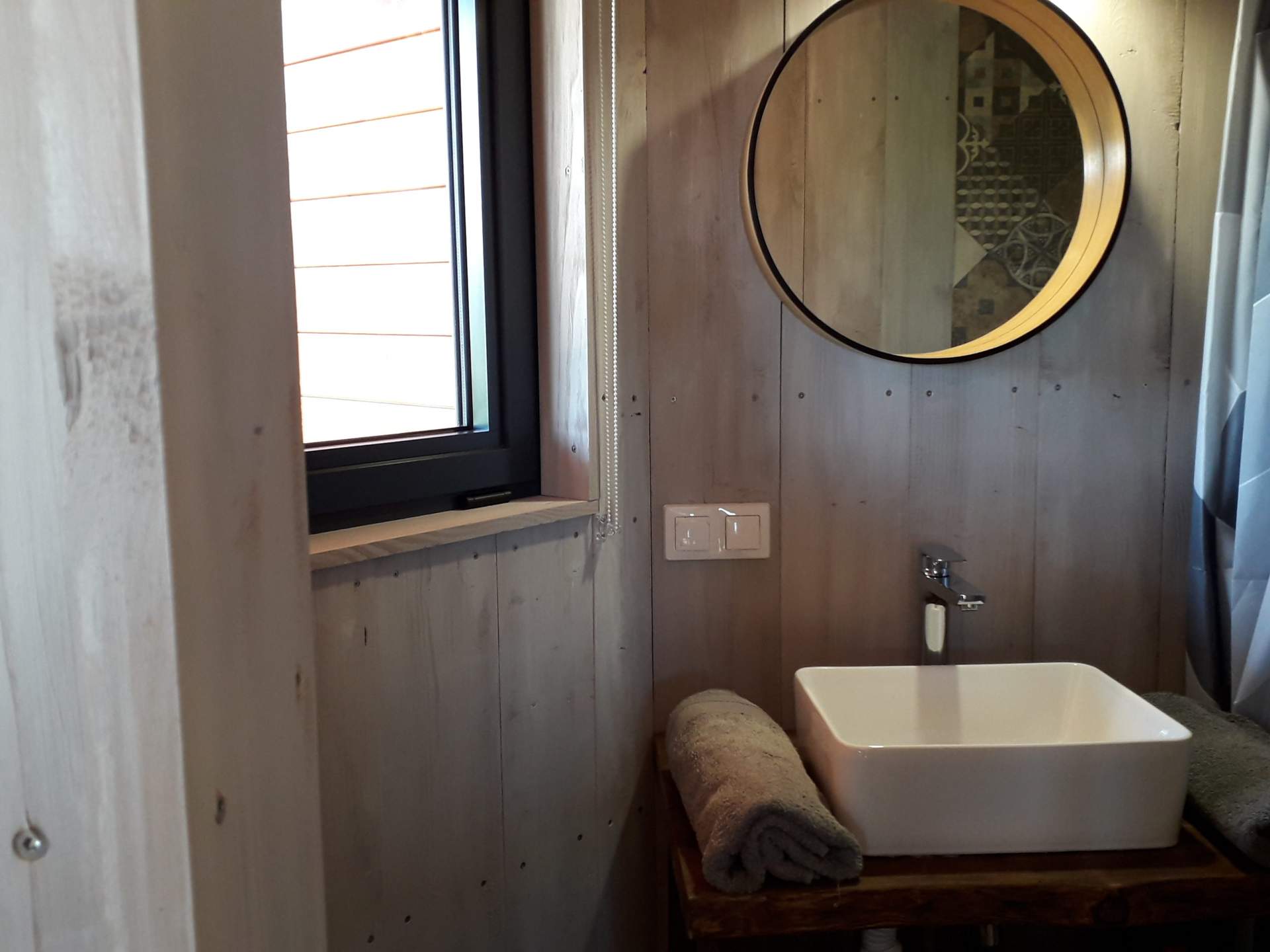 20201121_121609 Salle de bain moderne dans un hébergement insolite en bois, avec miroir rond et lumière naturelle.