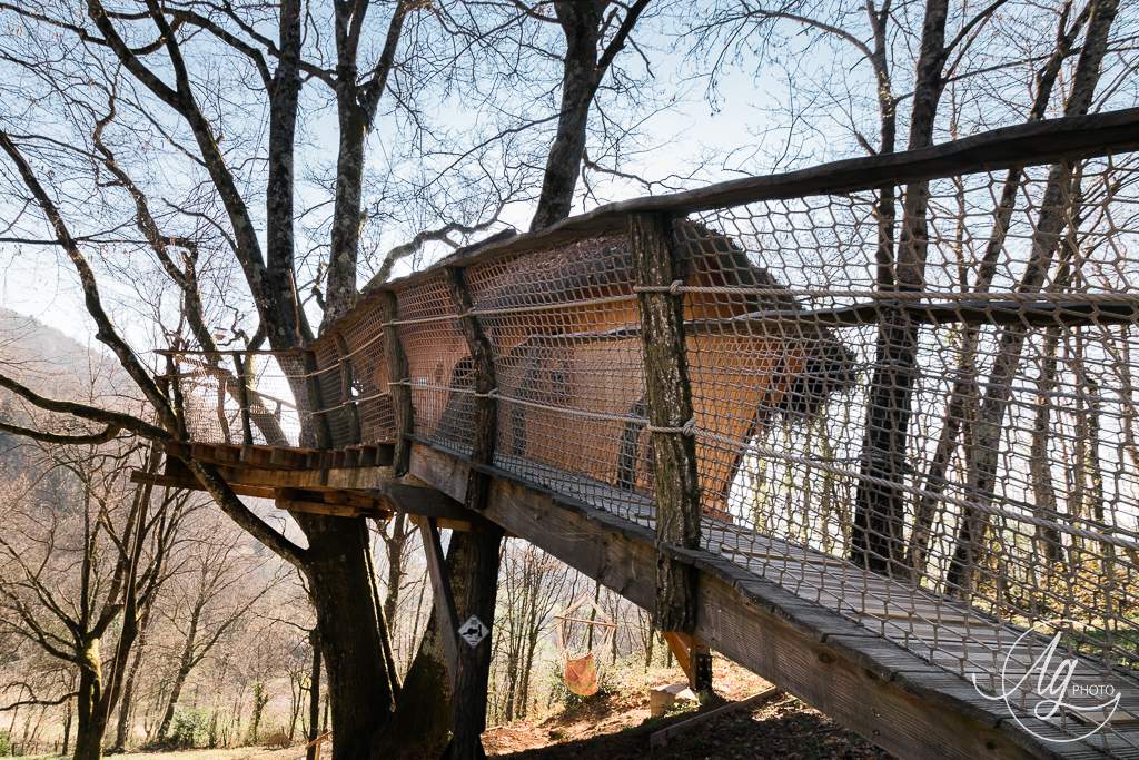 PE ext Cabane perchée dans les arbres, accessible par un pont en bois, entourée de nature.