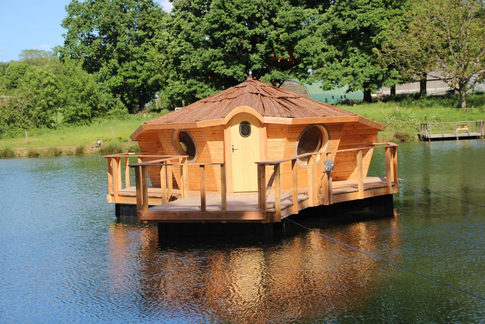 flottante ext 1 redim Cabane flottante en bois sur un lac, entourée de verdure luxuriante.