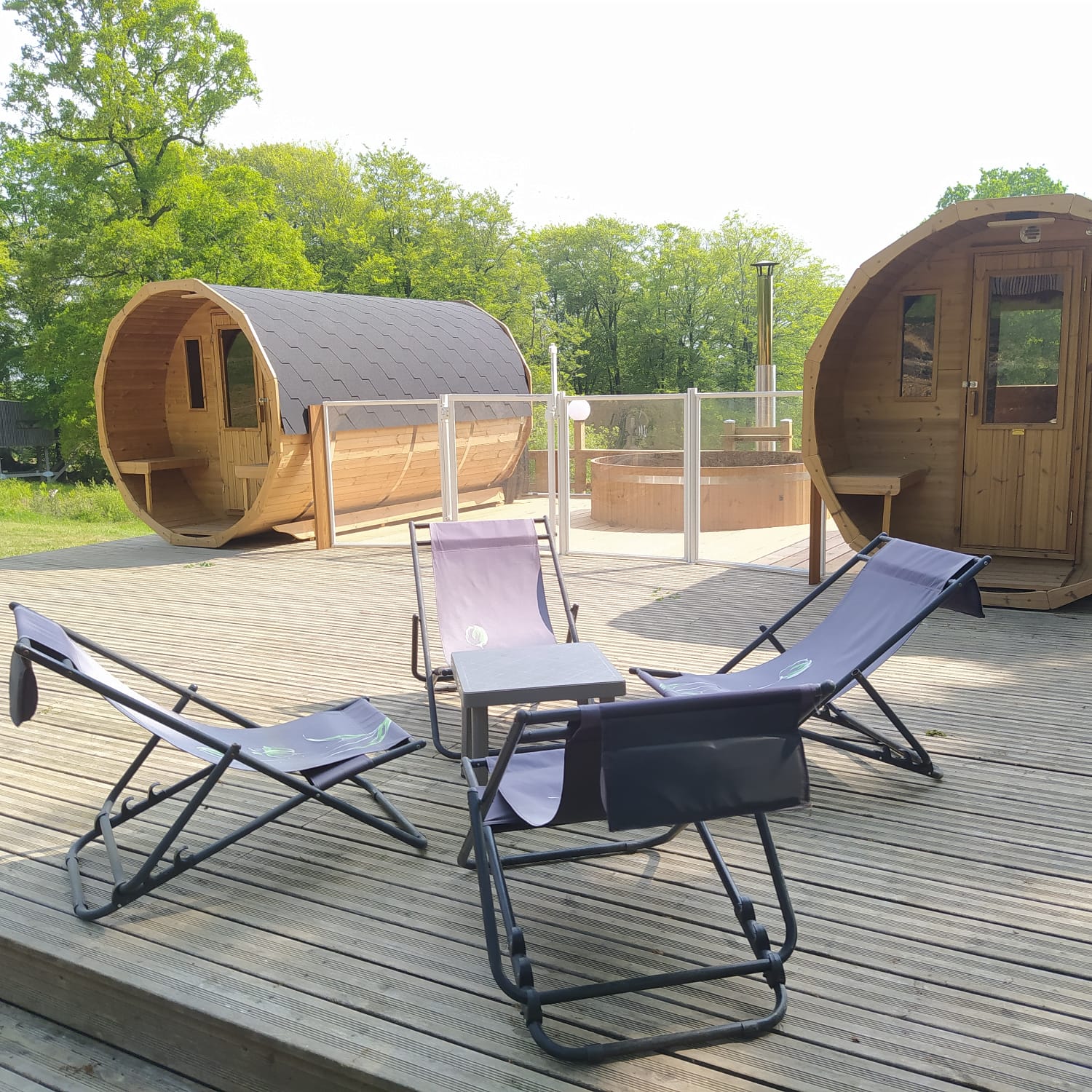 spa etape en foret Hébergement insolite en forme de tonneau avec terrasse et chaises longues.