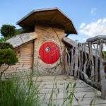 Hébergement insolite en forme de hobbit, porte rouge et cadre naturel verdoyant.
