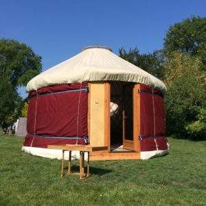 Yourte spacieuse avec une porte en bois, située dans un cadre verdoyant.
