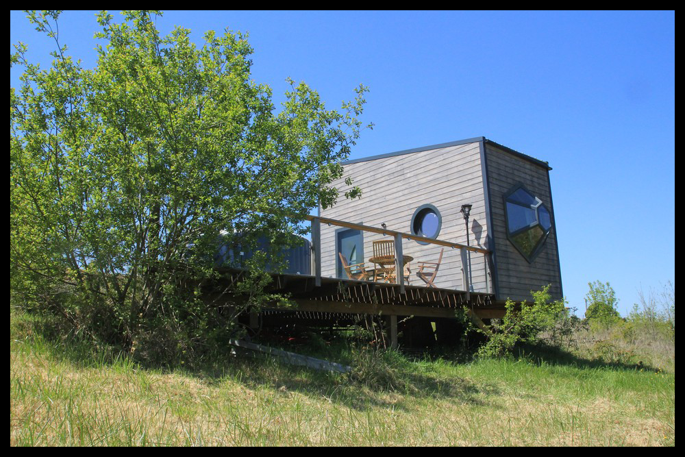 5 Cabane moderne sur pilotis, avec terrasse en bois et vue dégagée sur la nature.