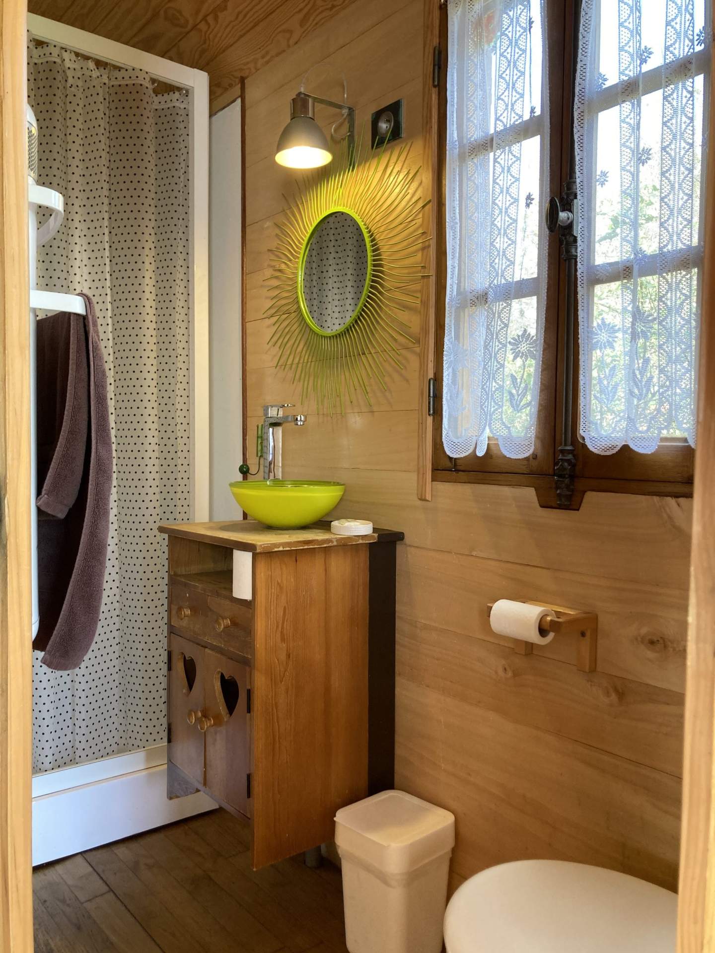 IMG_1617 Salle de bain dun hébergement insolite en bois, avec un miroir coloré et des fenêtres lumineuses.