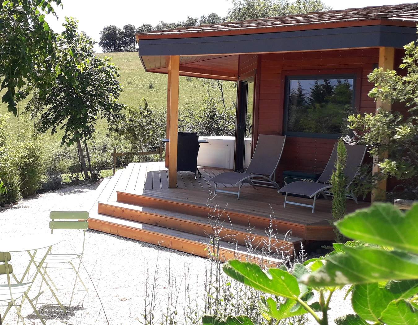 20210610_153849 - Copie Chalet en bois avec terrasse ensoleillée, entouré de verdure apaisante.