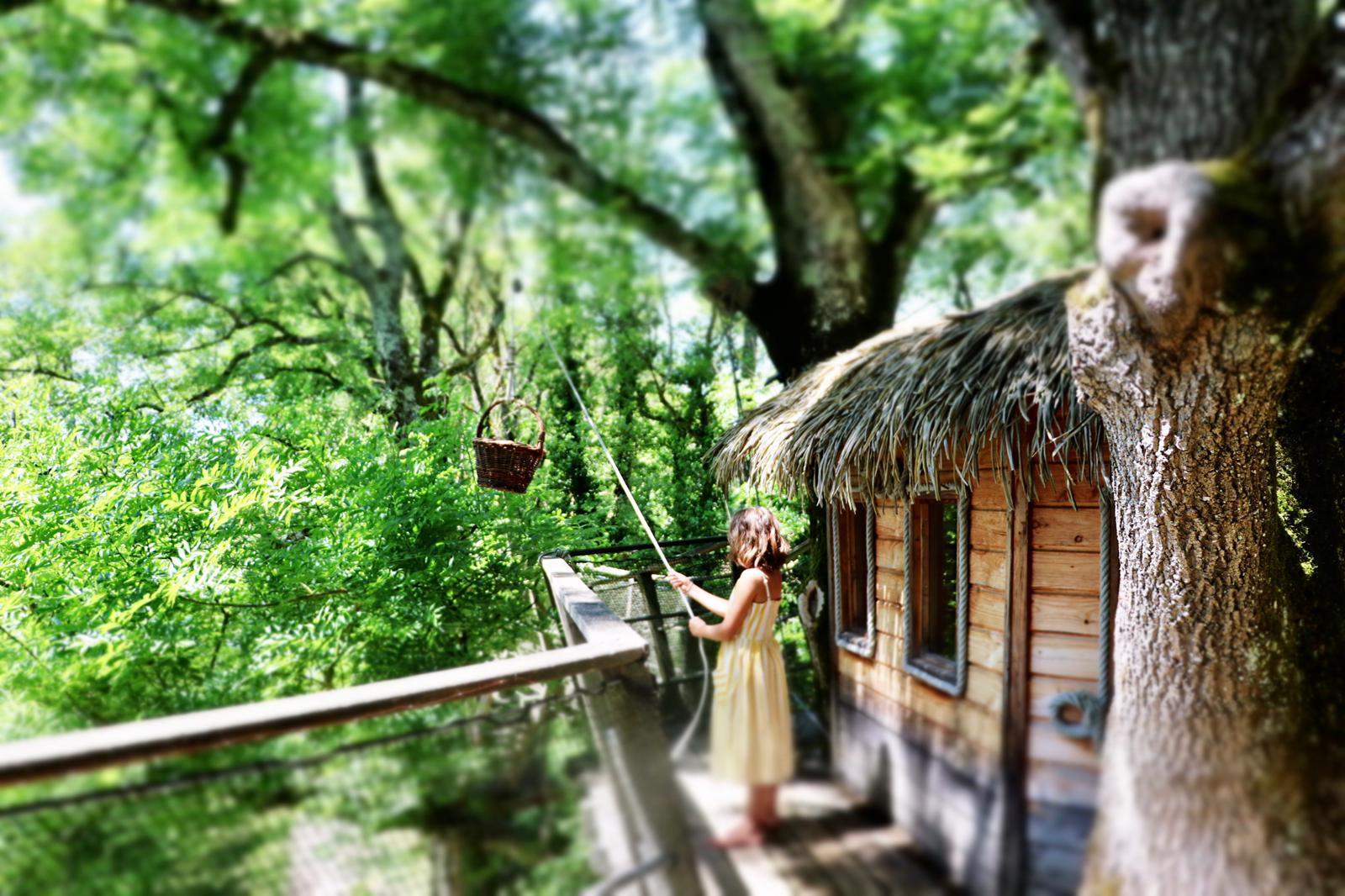 7c0e243a-df01-488b-849f-628a003ed0eb Cabane perchée dans les arbres, entourée de verdure, avec une petite fille et un panier.