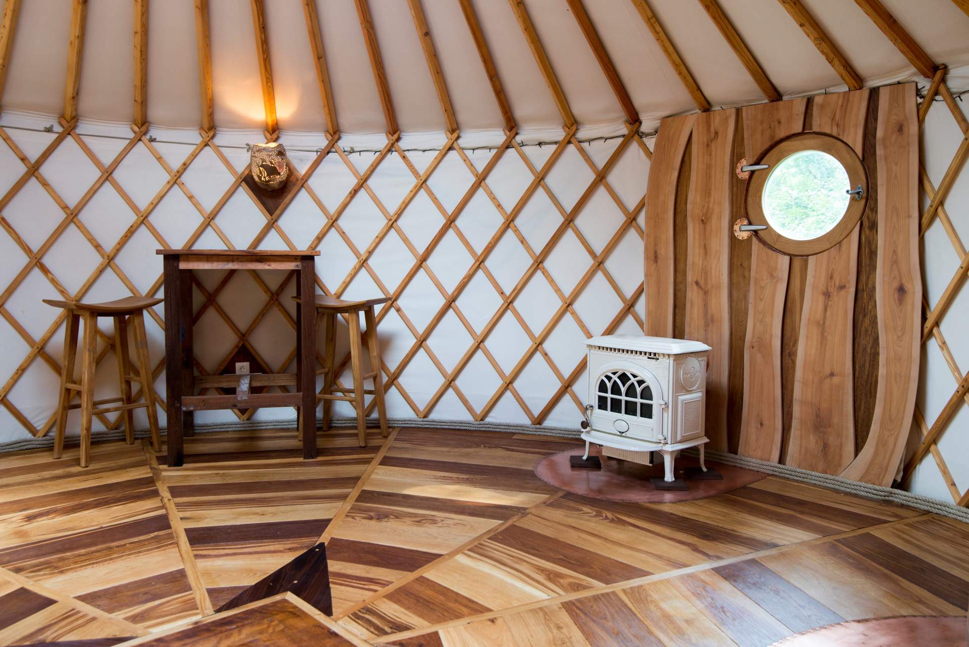 000_6107 Yourte en Bourgogne, intérieur en bois chaleureux avec un poêle vintage et une fenêtre ronde.