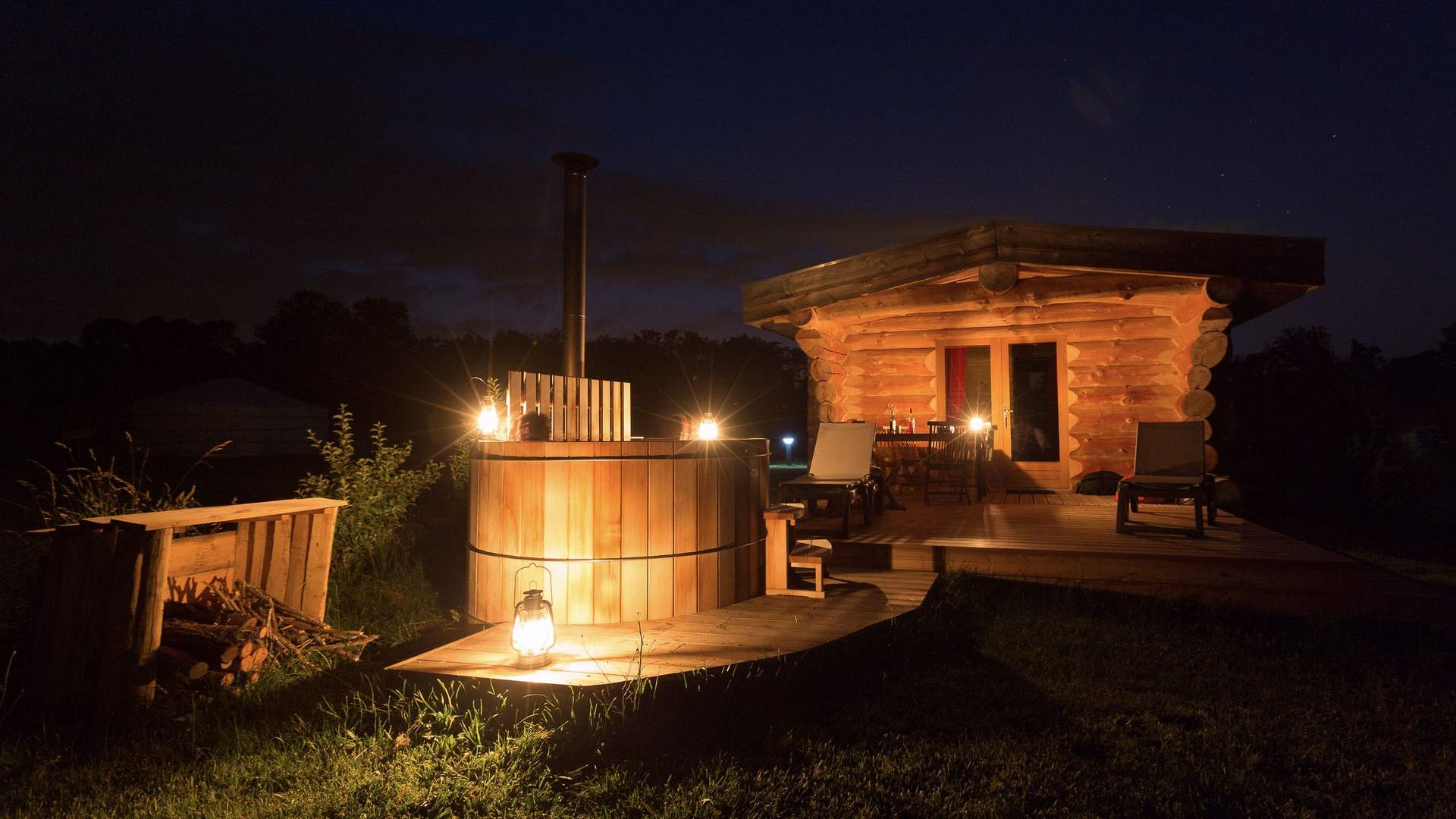 Cabane de trappeur spa 9 Cabane en bois avec un bain nordique, illuminée par des lanternes au crépuscule.