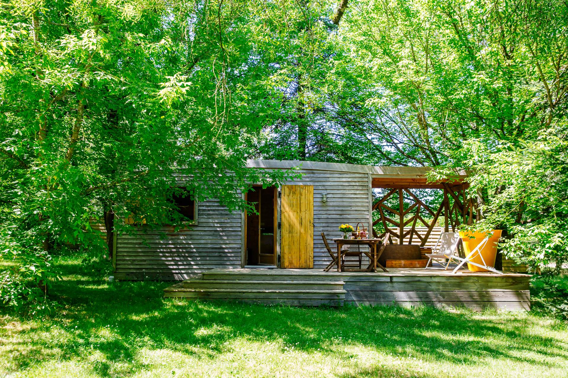 Oenolodge avec spa 1 Cabane en bois nichée dans la verdure, avec terrasse ensoleillée et mobilier extérieur.