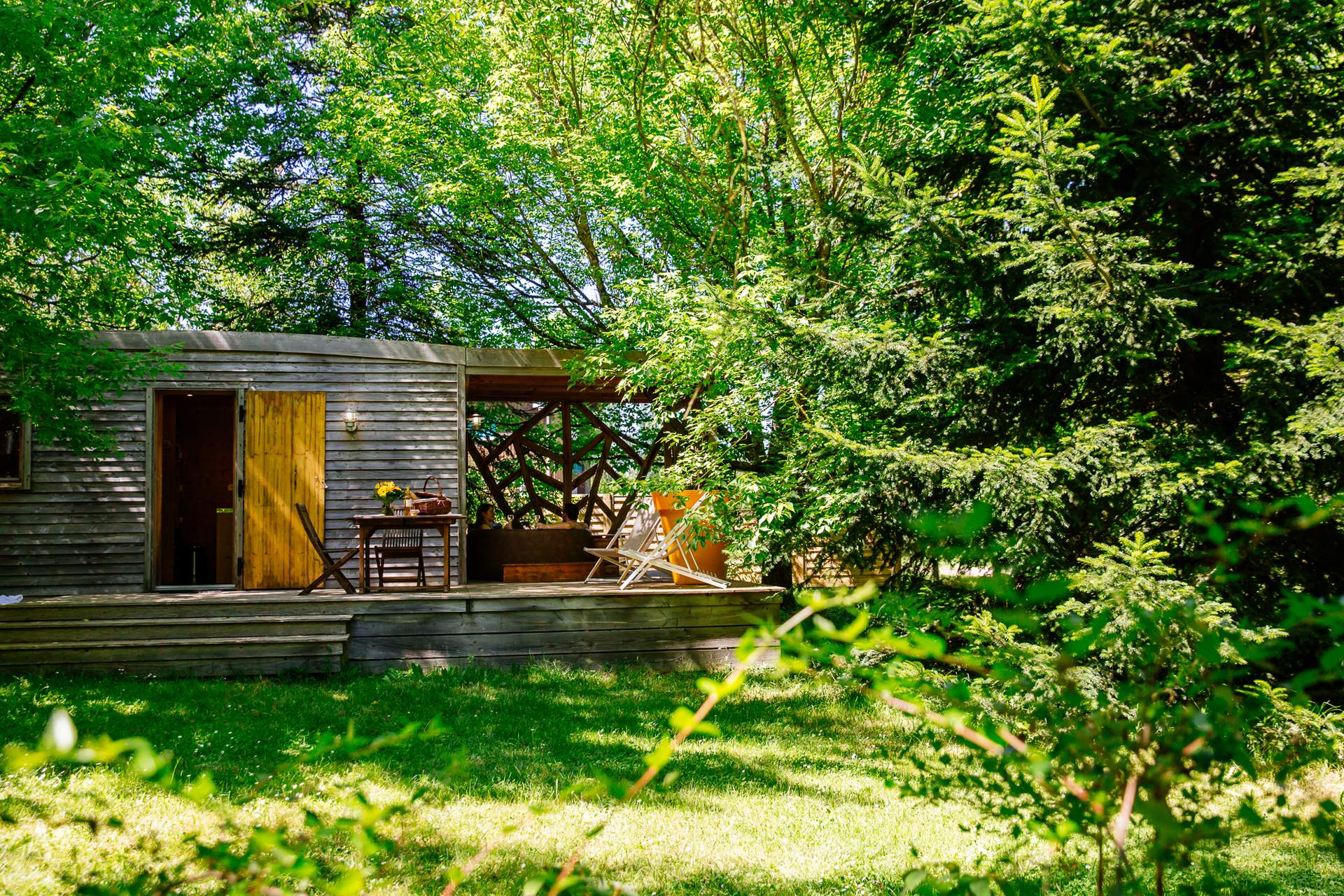 Oenolodge avec spa 8 Cabane en bois dans la verdure, avec une terrasse ensoleillée et des chaises confortables.