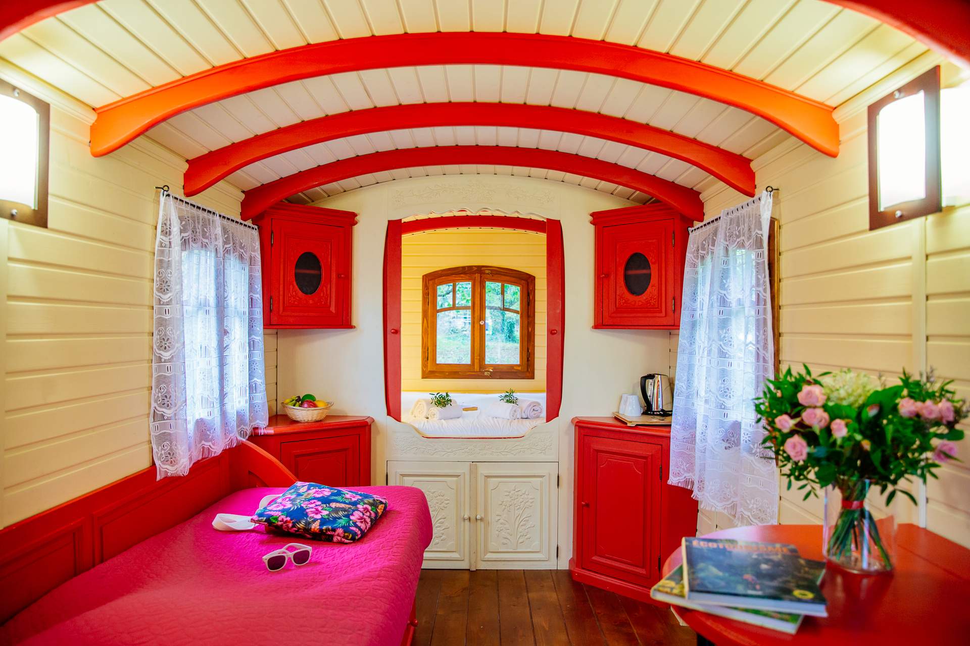 Roulotte Tzigane 5 Hébergement insolite en roulotte, intérieur cosy avec murs rouges et fenêtres lumineuses.
