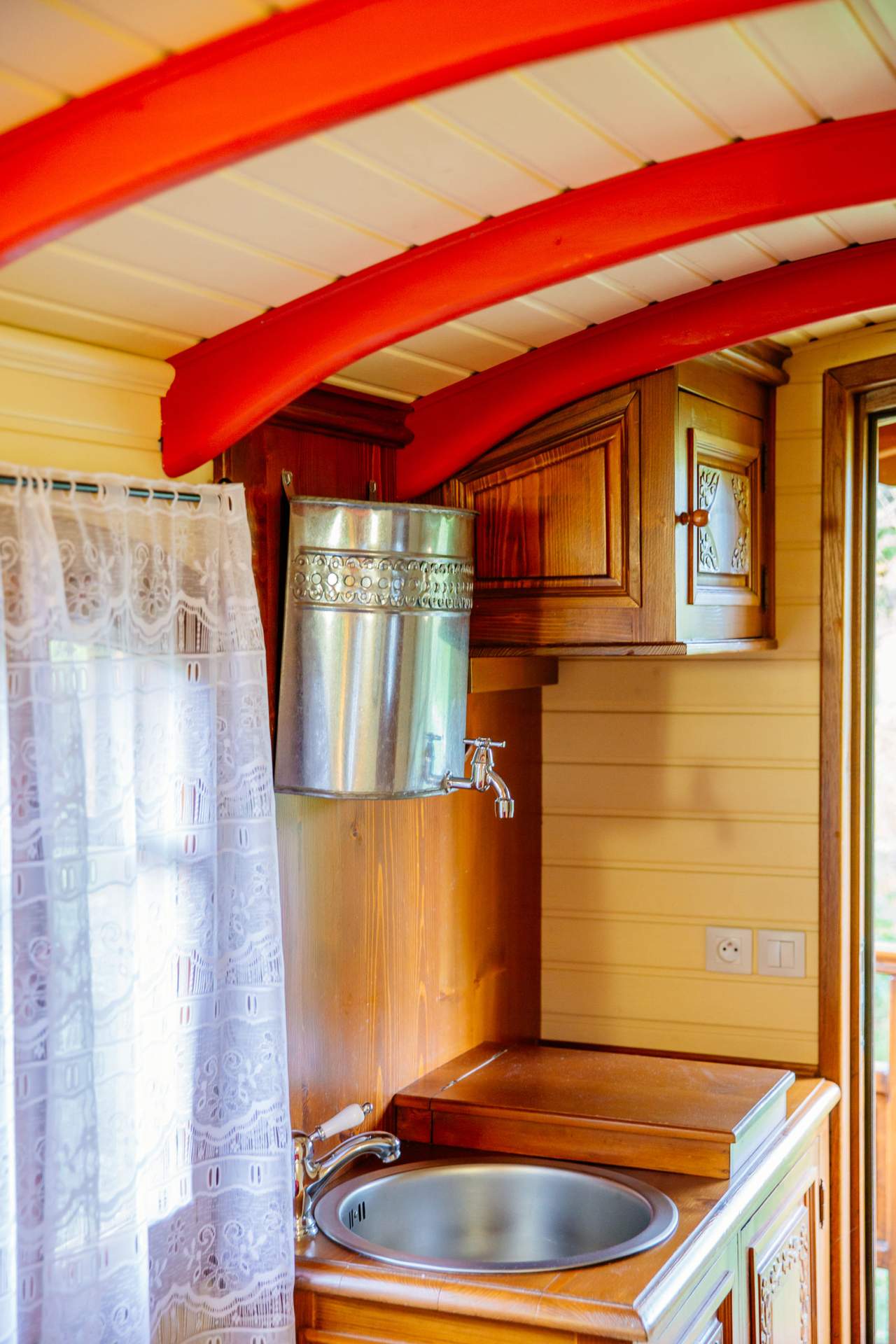 Roulotte Tzigane 7 Intérieur dune roulotte en Aquitaine, avec des poutres rouges et un évier en bois.