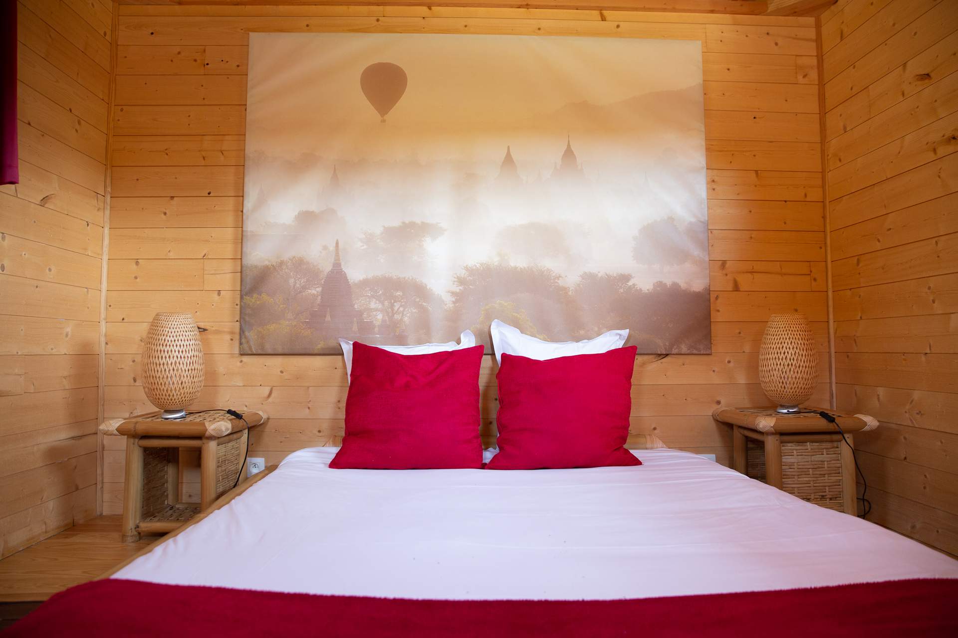 Temple perche avec spa 8 Chalet en bois avec lit douillet et coussins rouges, décoré dune grande toile.
