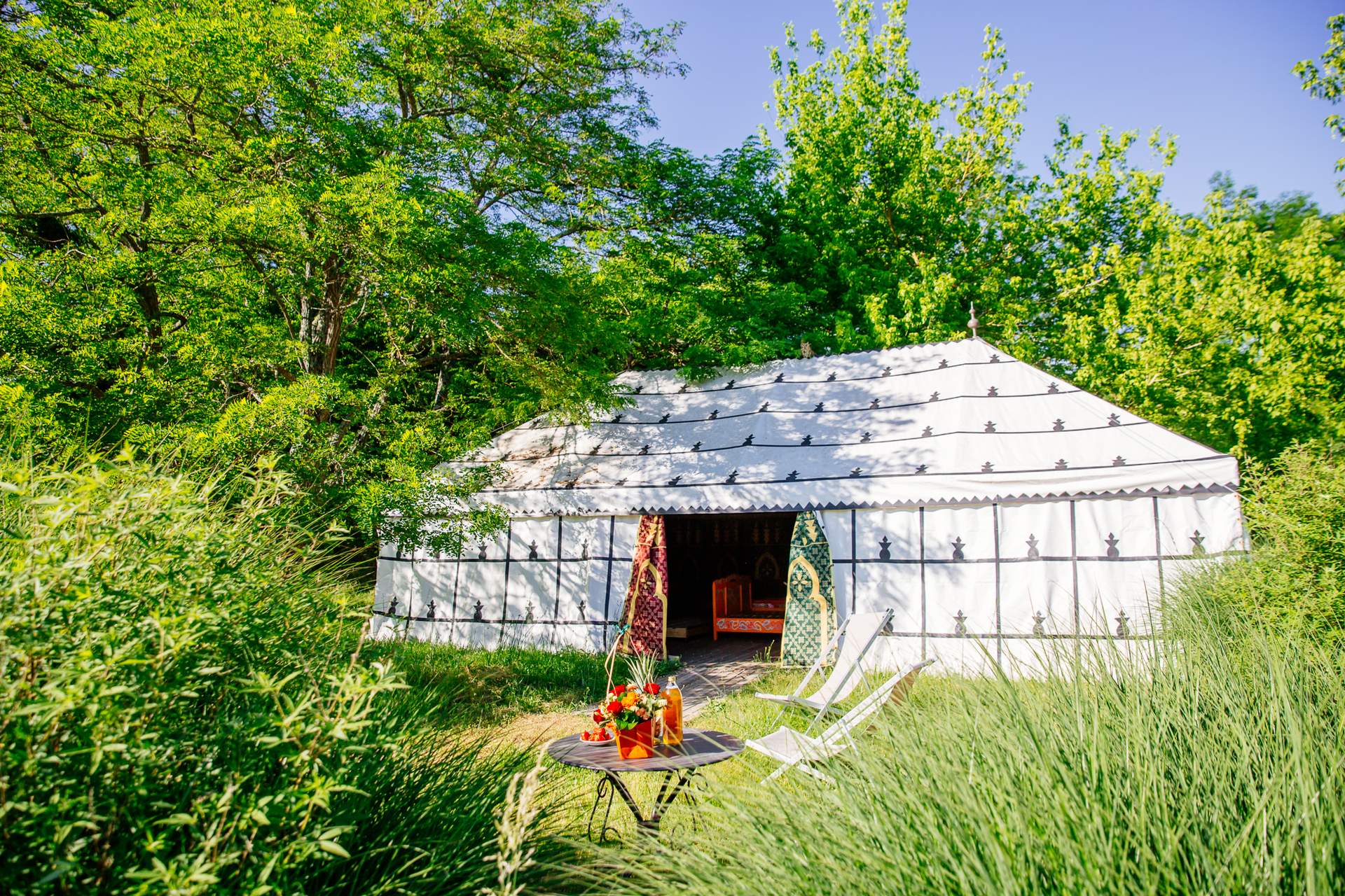 Tente Caidale 1 Yourte spacieuse en Aquitaine, entourée de verdure, avec chaises et table décorative.