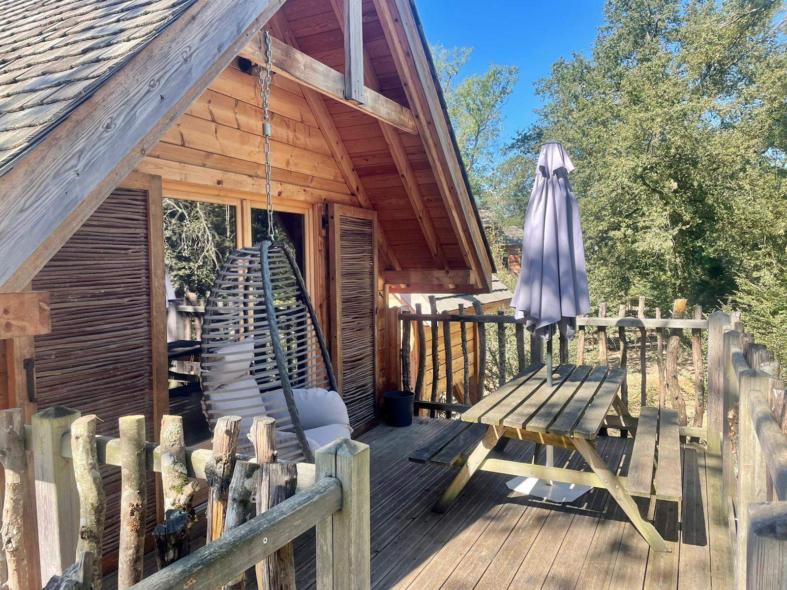 3b4dfcc2-9813-452b-ba86-3a03e4e79b5c Cabane perchée en Auvergne-Rhône-Alpes avec terrasse en bois et fauteuil suspendu.