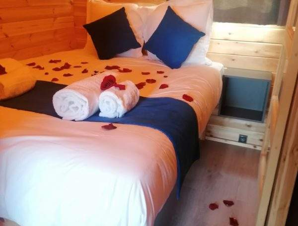 Chalet en bois romantique avec pétales de rose sur le lit et ambiance chaleureuse.