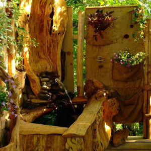 Cabane en bois avec un coin détente et une fontaine naturelle entourée de plantes.