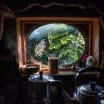 Cabane cosy avec fenêtre ronde, vue sur la verdure environnante.