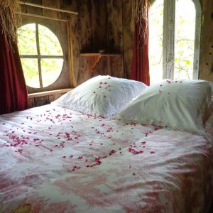 Chalet en bois avec lit romantique décoré de pétales de rose et fenêtres rondes.