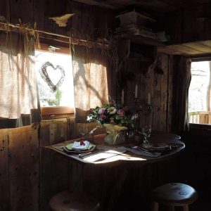 Cabane en bois avec une table décorée de fleurs et lumière douce à travers les fenêtres.