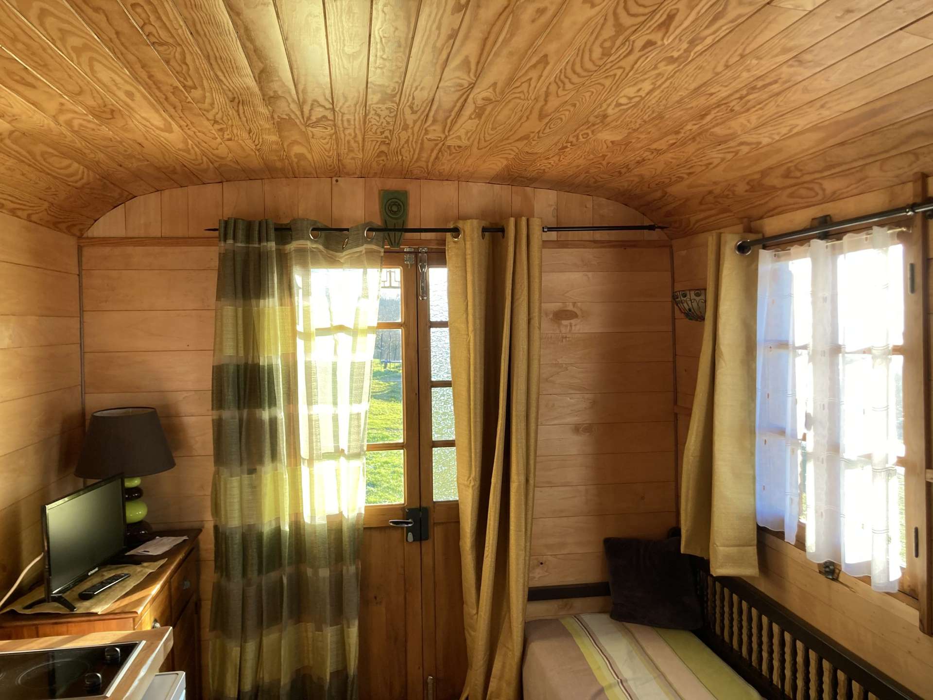 IMG_1551 Intérieur chaleureux dun hébergement insolite en bois, avec lumière naturelle et rideaux colorés.