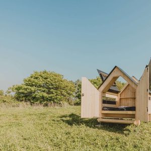 Cabane en bois avec toit ouvert, située dans un champ verdoyant.