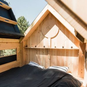 Cabane en bois avec lit douillet et fenêtres laissant entrer la lumière naturelle.