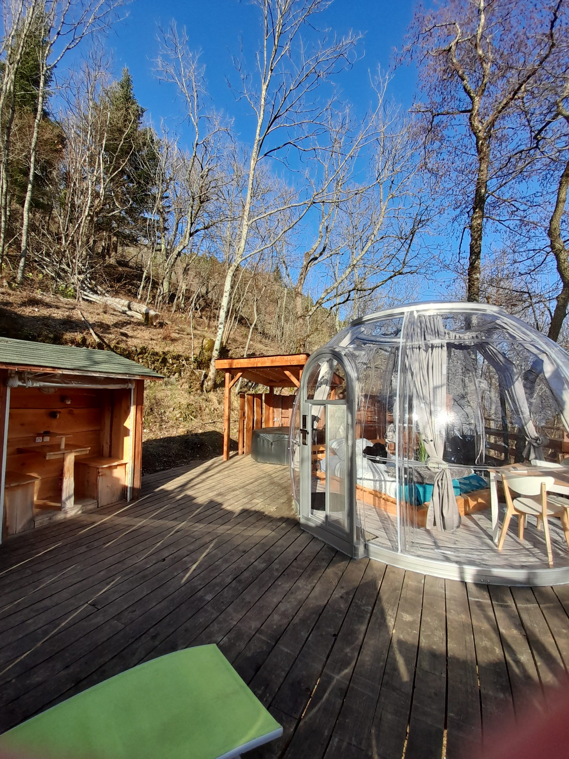 20220210_152937 Hébergement insolite en bulle transparente, entouré darbres, avec terrasse en bois.