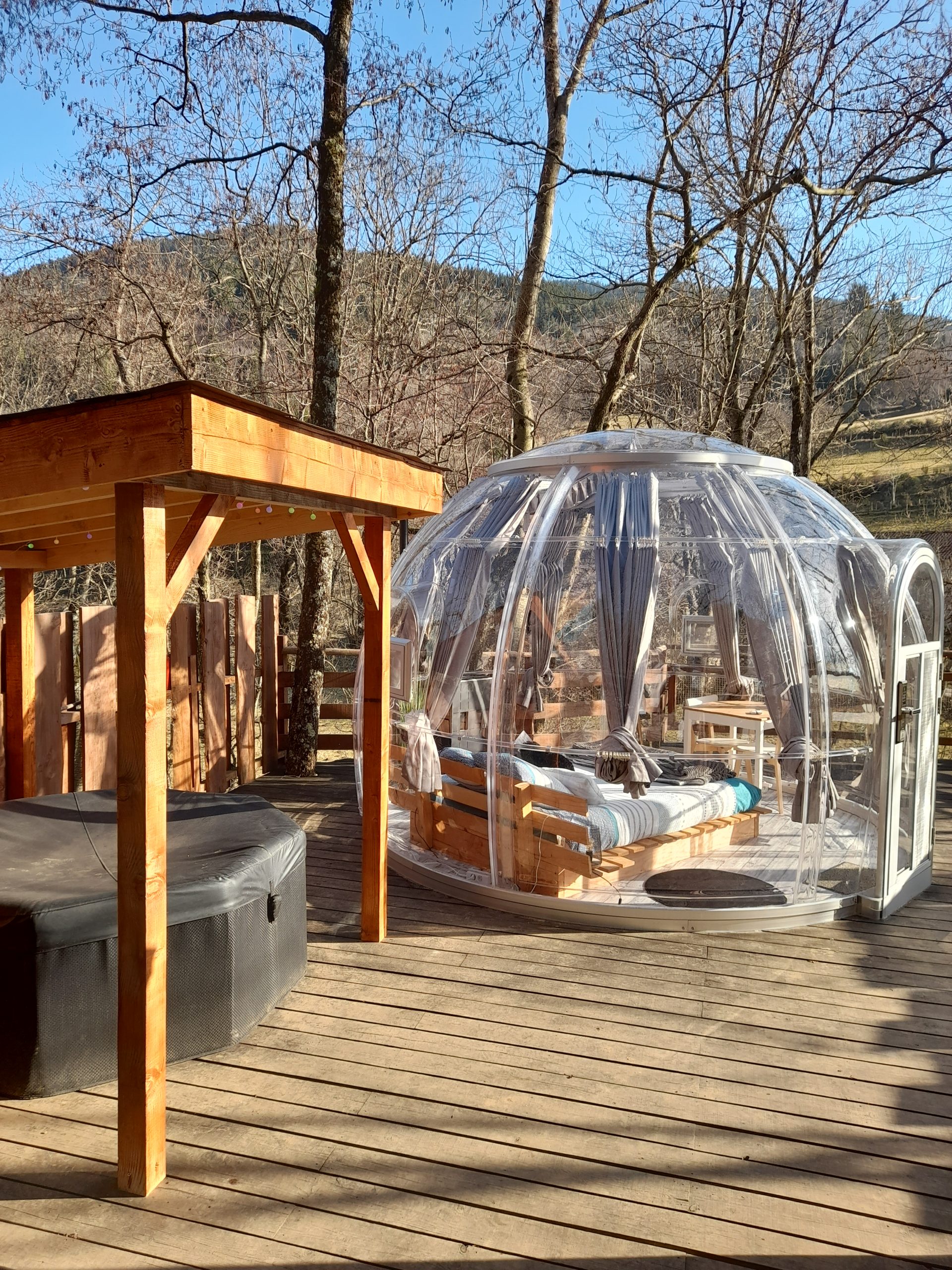 20220210_153021 Hébergement insolite en bulle transparente, avec un lit et un coin détente en bois.
