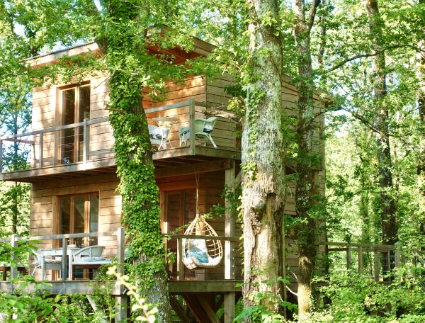 Cabane perchée en bois, entourée darbres, avec balcon et chaises confortables.