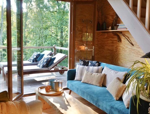 Cabane en bois avec terrasse, salon lumineux et vue sur la nature verdoyante.