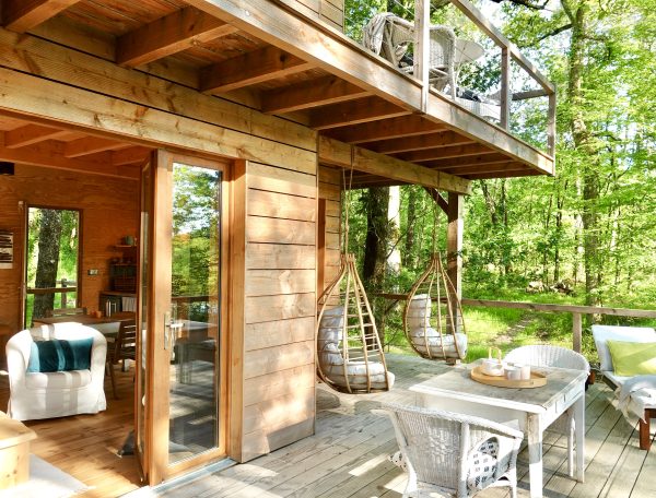 Cabane en bois dans les arbres, avec balançoires suspendues et vue sur la forêt.