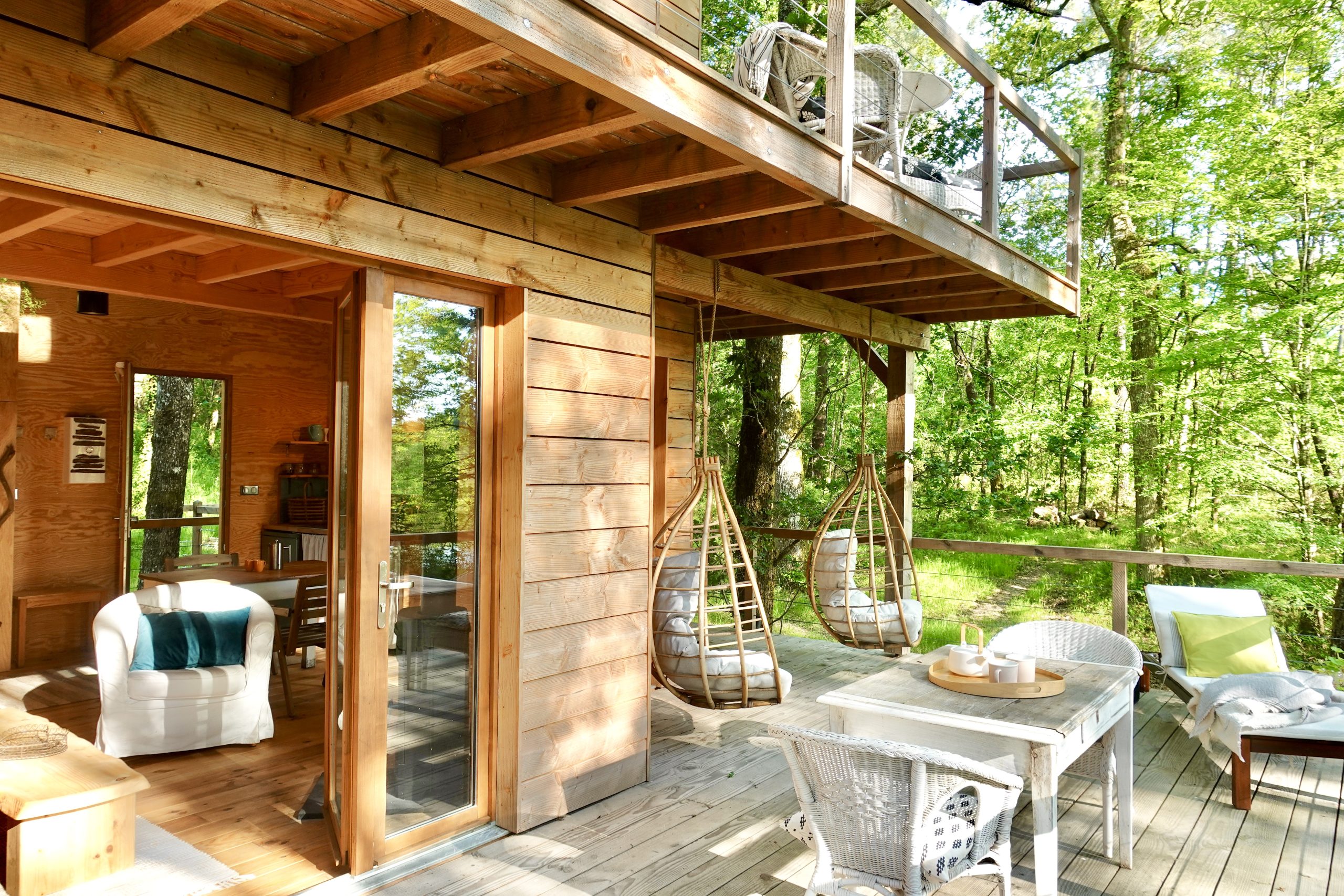 Cabane en bois dans les arbres, avec balançoires suspendues et vue sur la forêt.