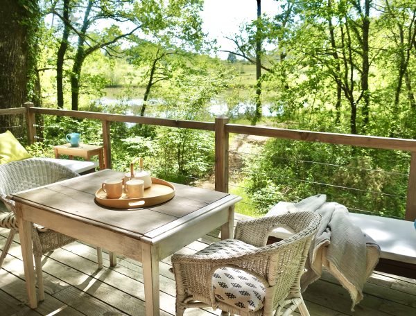 Cabane en bois avec terrasse, vue sur la nature verdoyante et le lac.