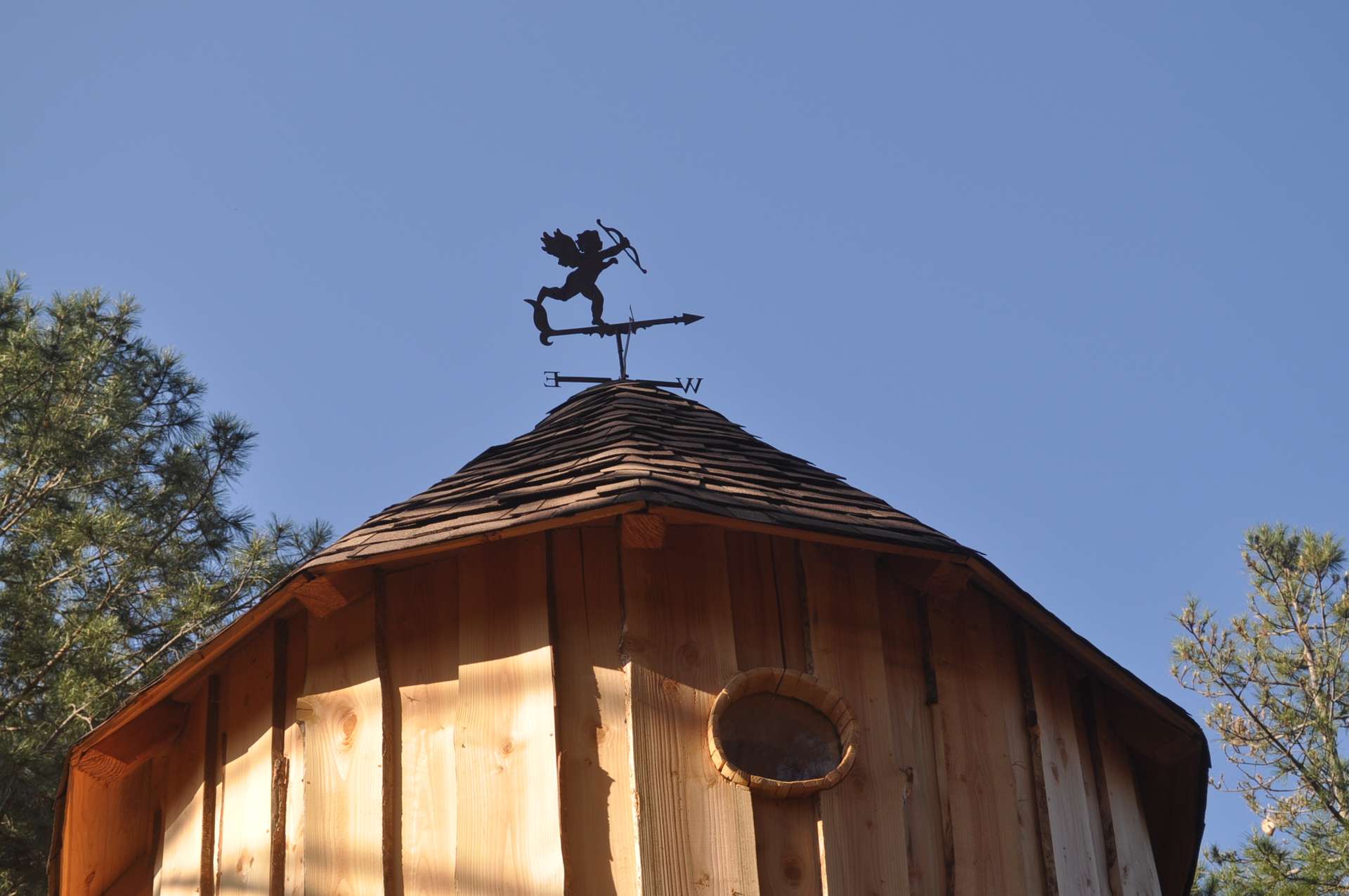 DSC_0073 Cabane en bois avec un toit conique et une girouette en métal au sommet.