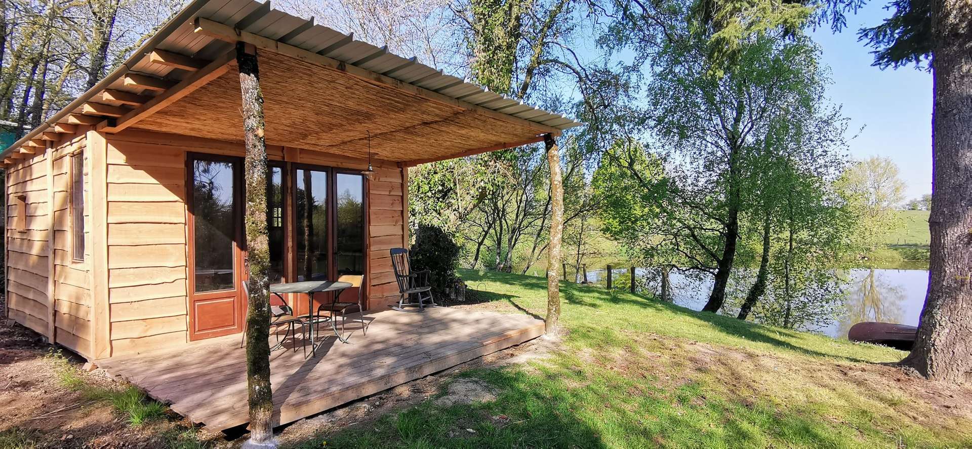 IMG_20210421_101749 Cabane en bois au bord dun lac, avec terrasse et vue sur la nature verdoyante.