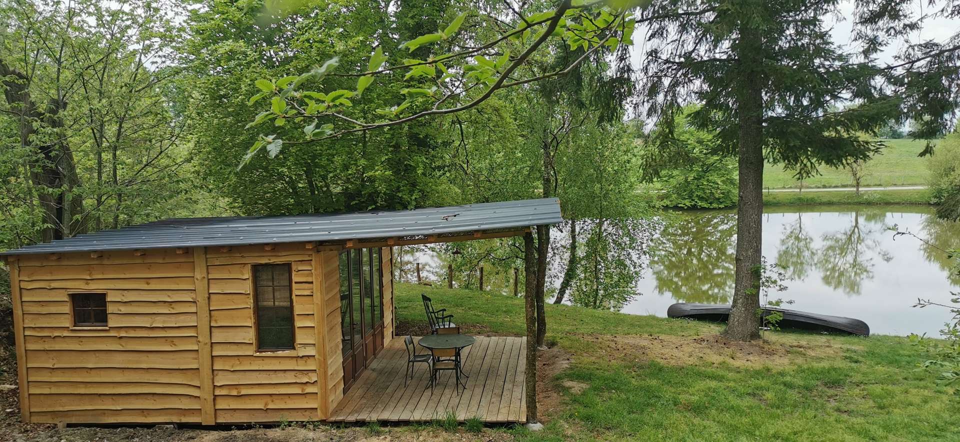IMG_20210430_132643 Cabane en bois au bord dun étang, entourée de verdure et dun coin salon extérieur.