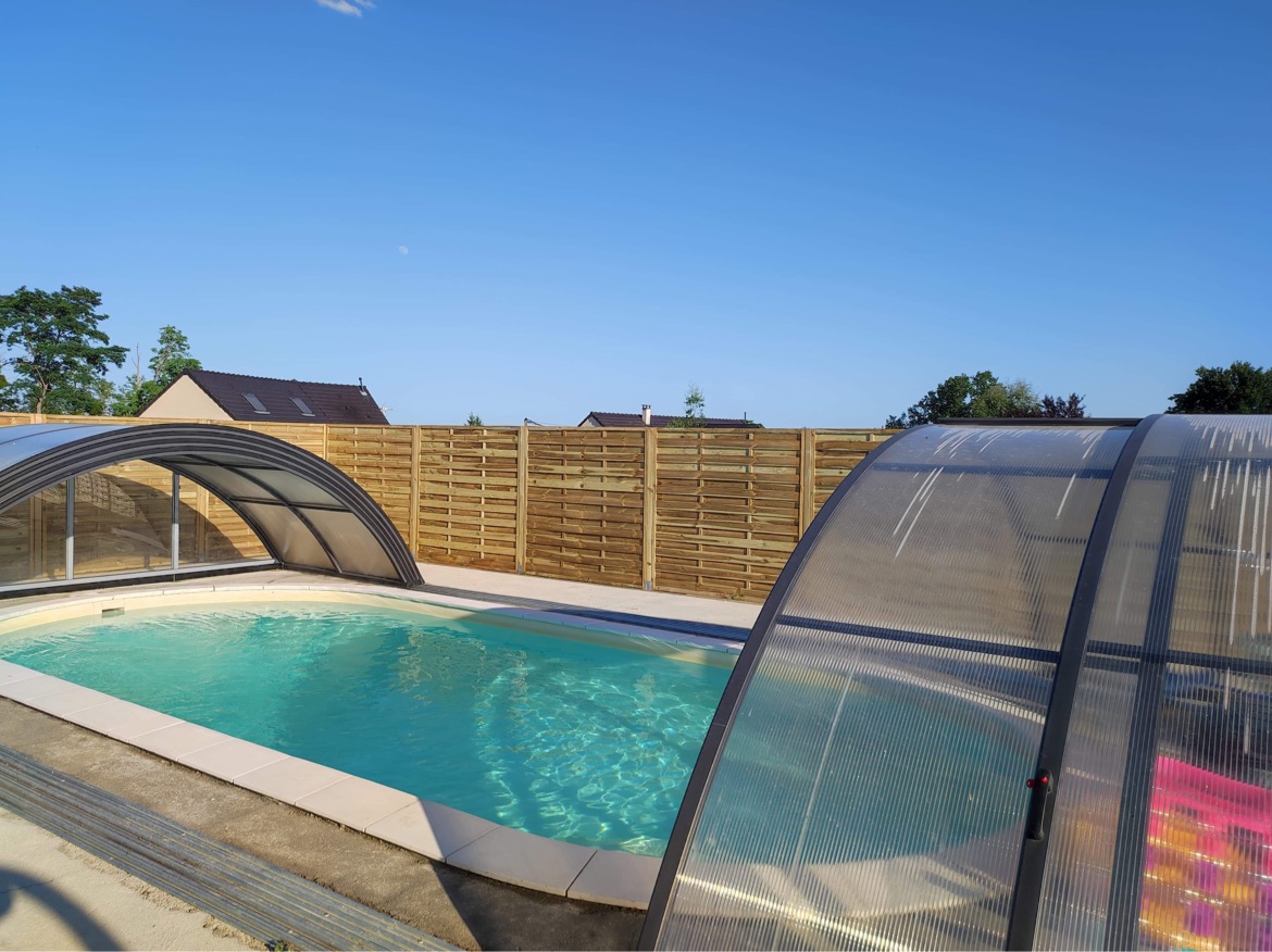 9E0DB920-7A16-45C2-9254-E9E651853F9C Hébergement insolite avec piscine couverte, entouré dune clôture en bois.