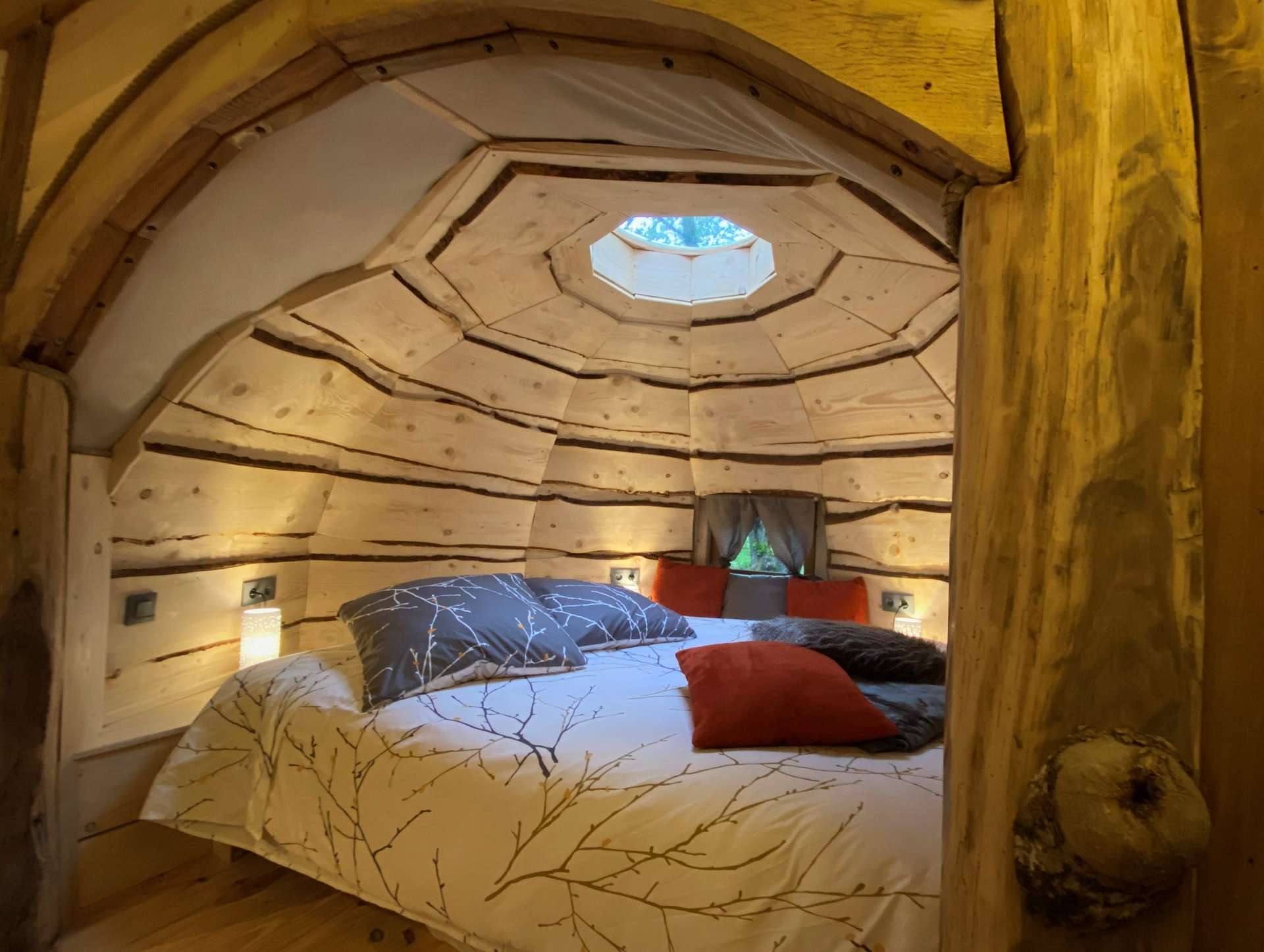 IMG_5603 Cabane en bois avec un lit douillet, éclairage doux et fenêtre circulaire.