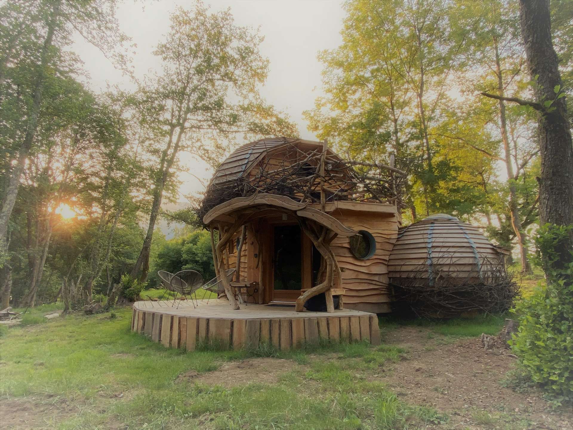 IMG_5971 Cabane en bois originale, entourée darbres, avec un toit en forme de dôme.