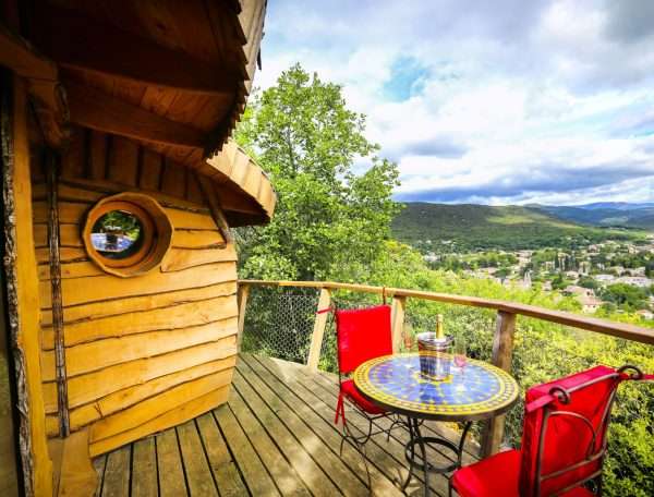 Cabane perchée avec vue panoramique, terrasse en bois et table colorée.