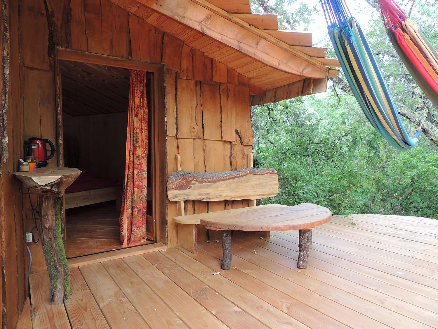 inattendue2 Cabane perchée en bois avec hamacs, offrant une vue sur la nature verdoyante.