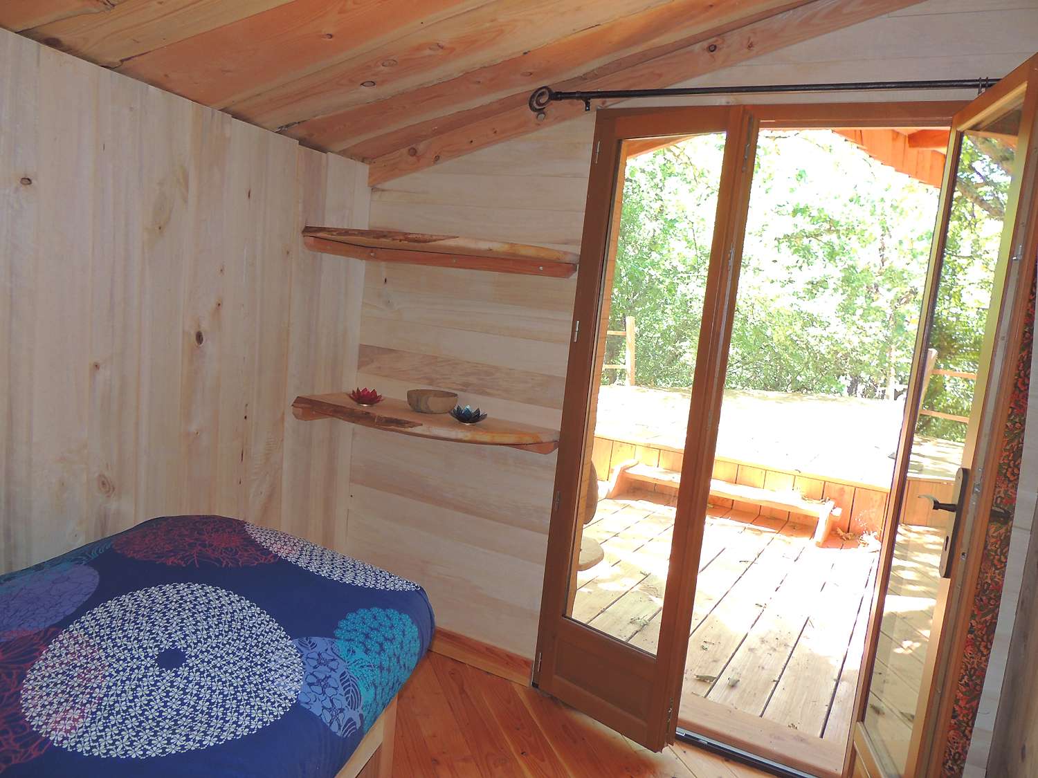 inattendue6 Chalet en bois avec lit coloré et accès à une terrasse ensoleillée.