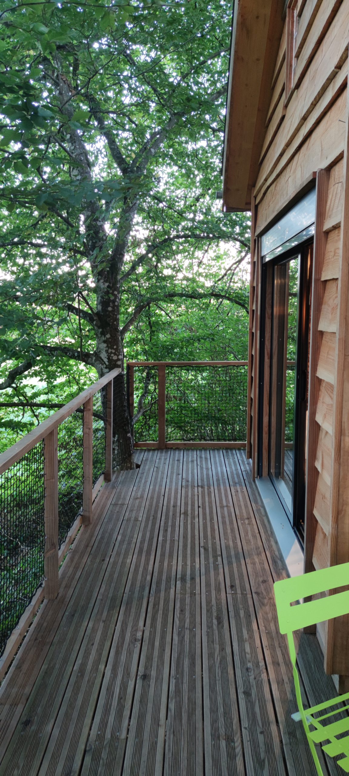 IMG_20210930_185427 Cabane perchée en bois avec terrasse en bois, entourée de verdure luxuriante.