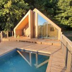 Cabane moderne avec piscine, entourée de verdure et grandes baies vitrées.