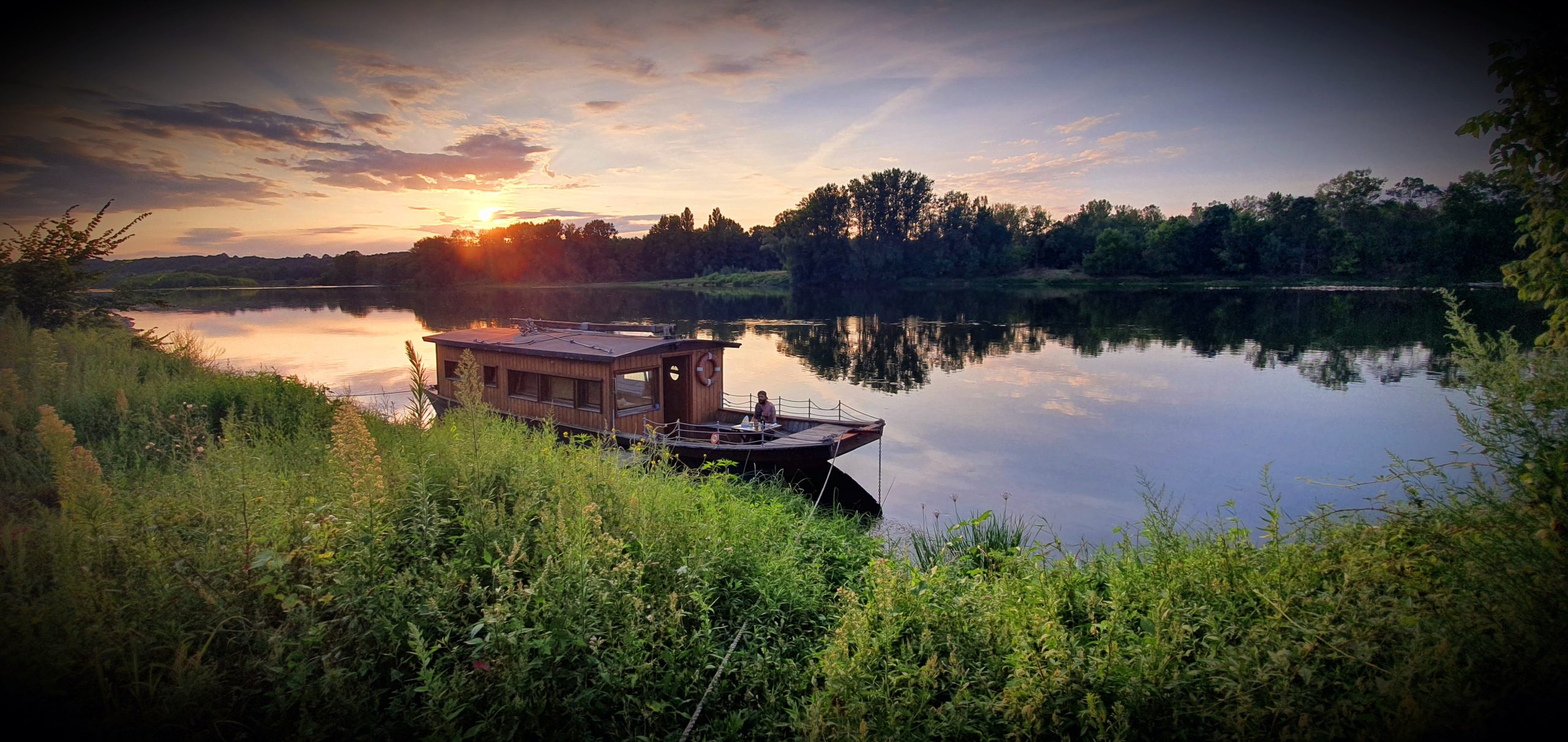 20200815_224131 Bateau-hôtel sur la Loire, au coucher de soleil, entouré de verdure paisible.