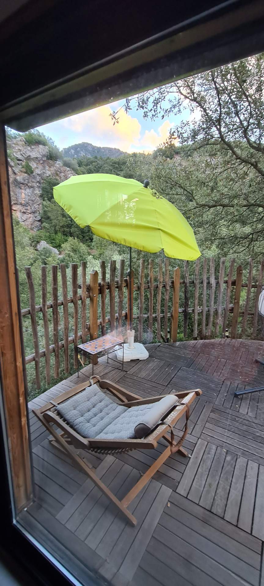 20220828_193123 Hébergement insolite en Corse : terrasse en bois avec un transat et un parasol vert.