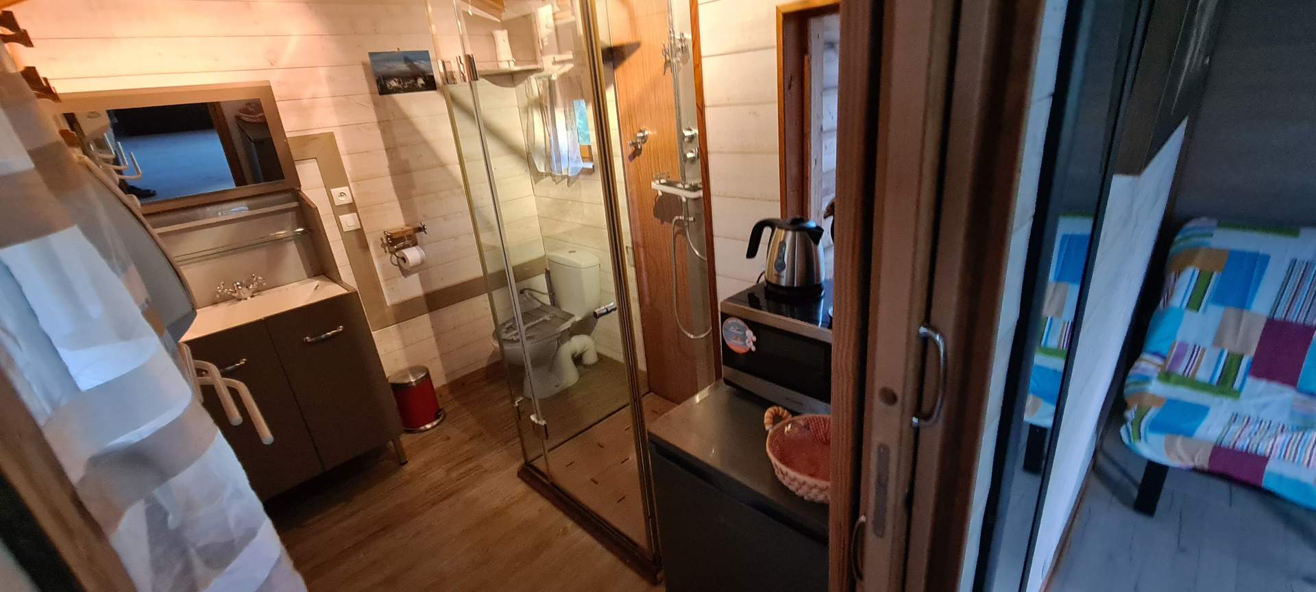 Hébergement insolite en Corse : intérieur moderne avec douche vitrée et lit coloré.