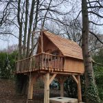 Cabane dans les arbres en bois, perchée entre les arbres avec un balcon accueillant.